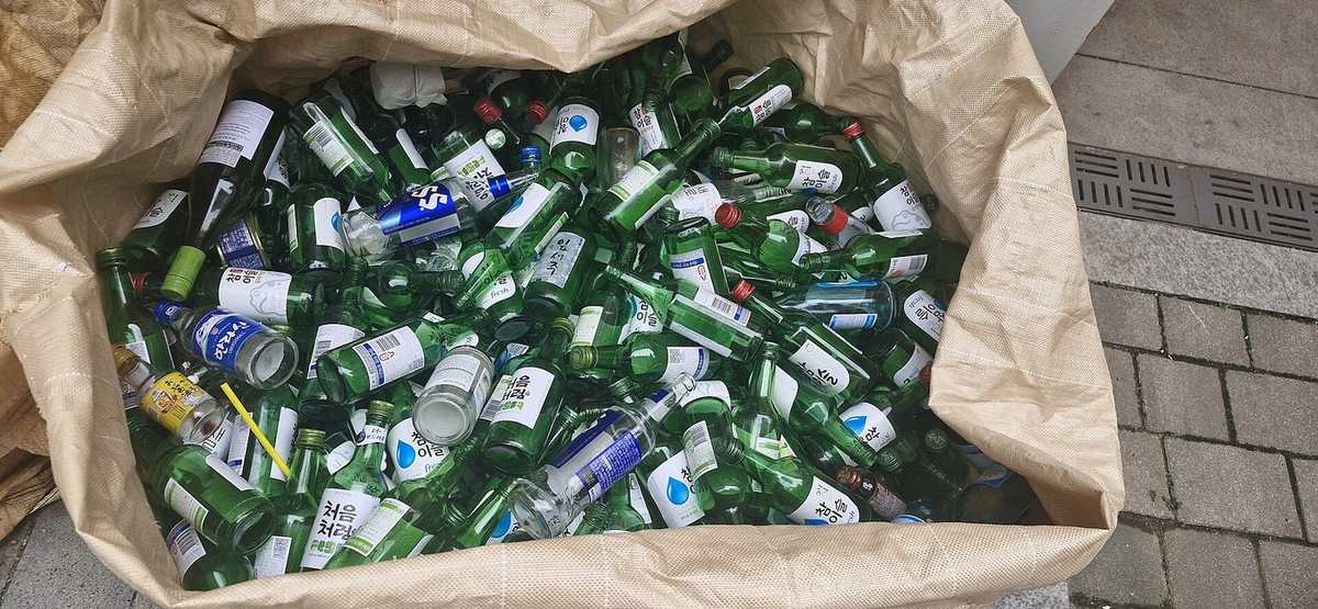 Bags of empty green soju bottles collected for glass recycling near an apartment complex in Korea — soju highball global