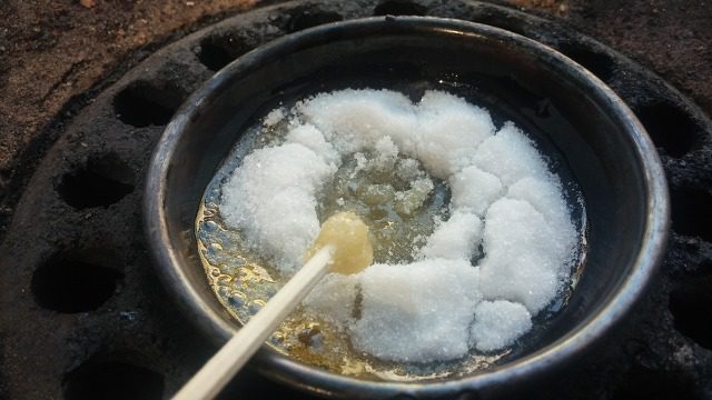 Sugar melting in a metal ladle over a burner to make Korean dalgona candy